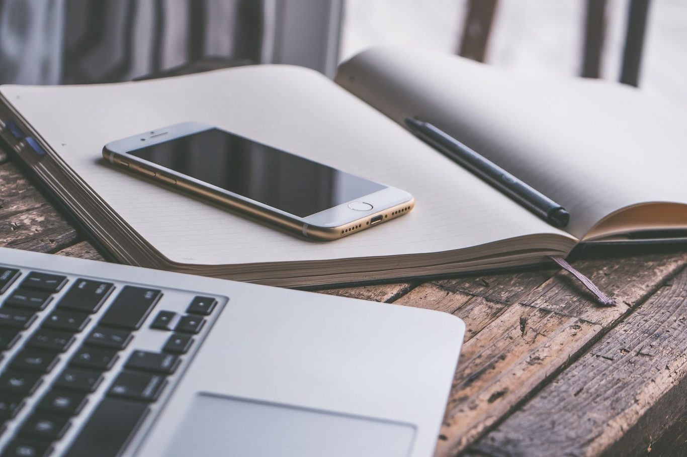 Notizbuch, Mobiltelefon und Notebook Ein aufgeklapptes Notizbuch, daruf liegt ein Mobiltelefon. Teile eines Notebooks sind zu erkennen.